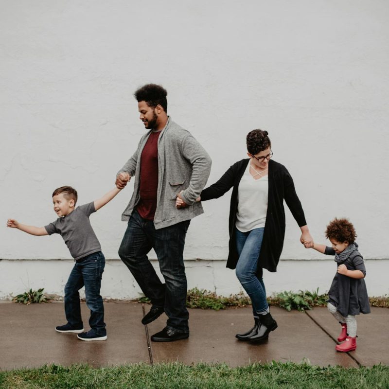 A joyful family walking together outdoors, holding hands in a playful and happy moment.